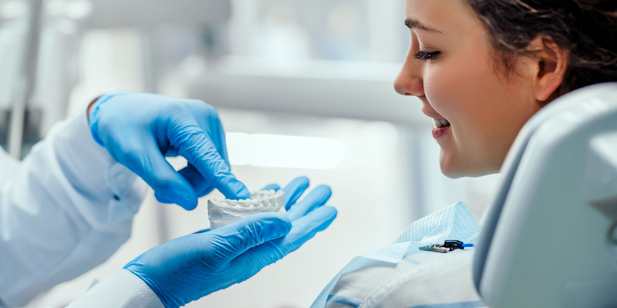 Male dentist showing his female patient how to brush teeth correctly, using dental mold. Mature woman watching her dentist explaining about teeth and gums care.