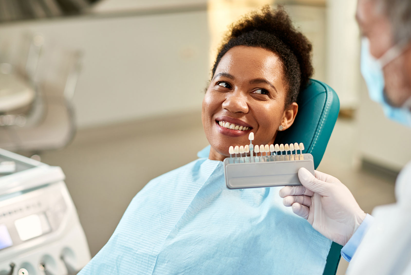woman and her dentist choosing shade of dental veneers during appointment at dentist's office.